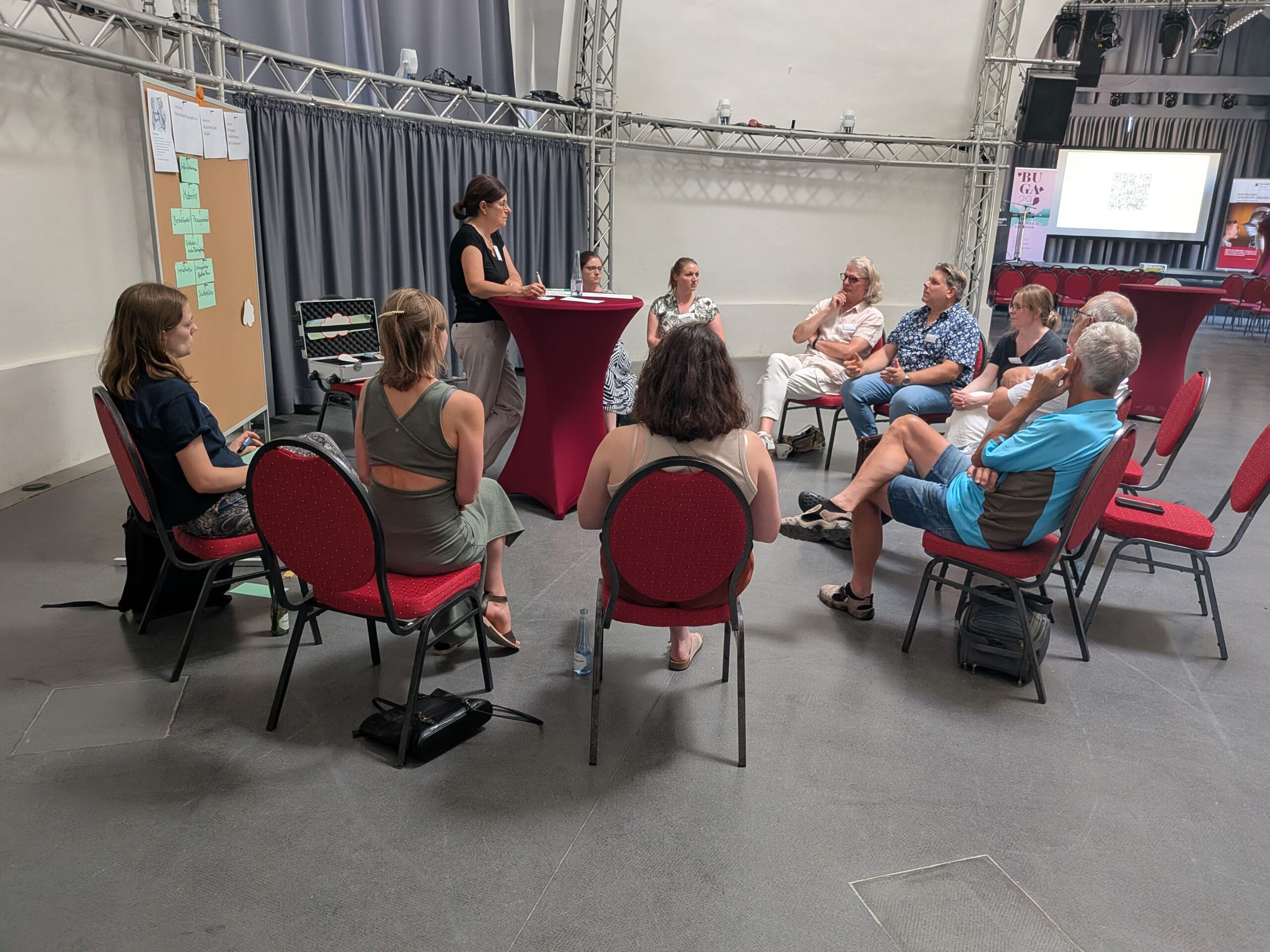 20250703_PM_Foto2 Eine Gruppe von Menschen sitzt auf Stühlen in einem Kreis um eine vortragende Person.