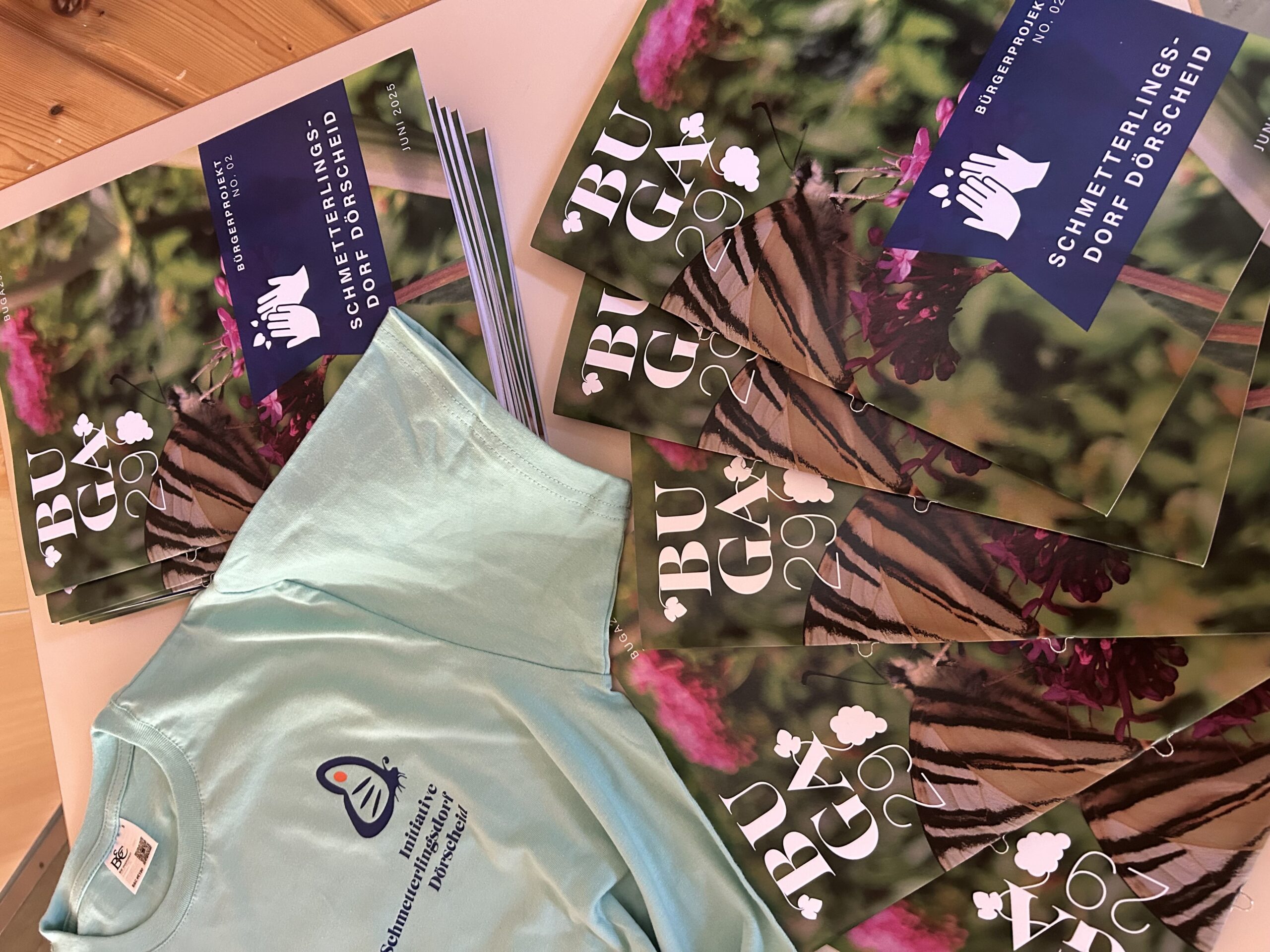 sliderimage-Mit Broschüre und T-Shirt informiert die Initiative „Schmetterlingsdorf Dörscheid“ über ihr Konzept und lädt zur aktiven Mitgestaltung ein.