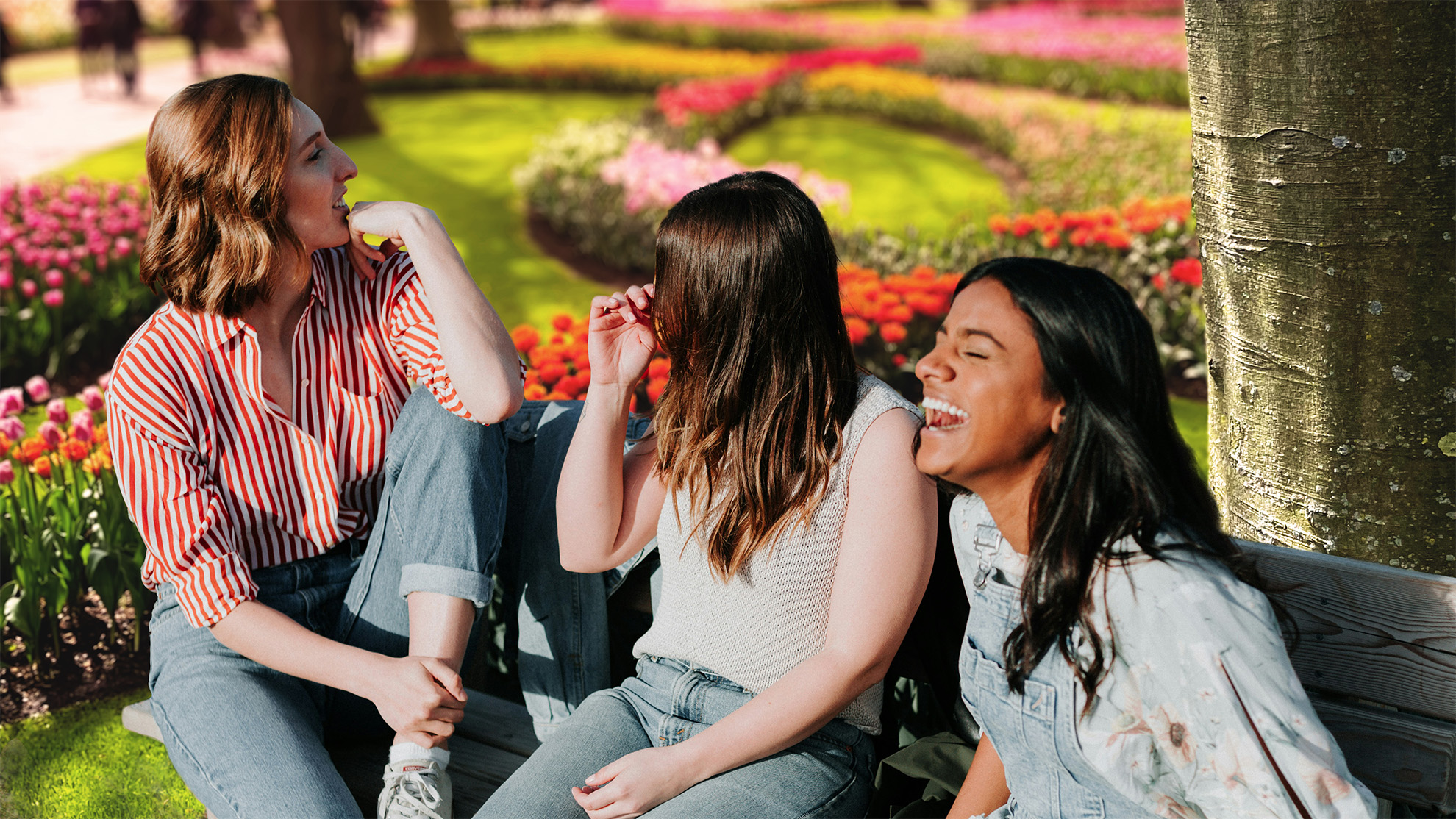 Drei Frauen sitzen auf einer Bank vor einem bunten Park voller Blumen