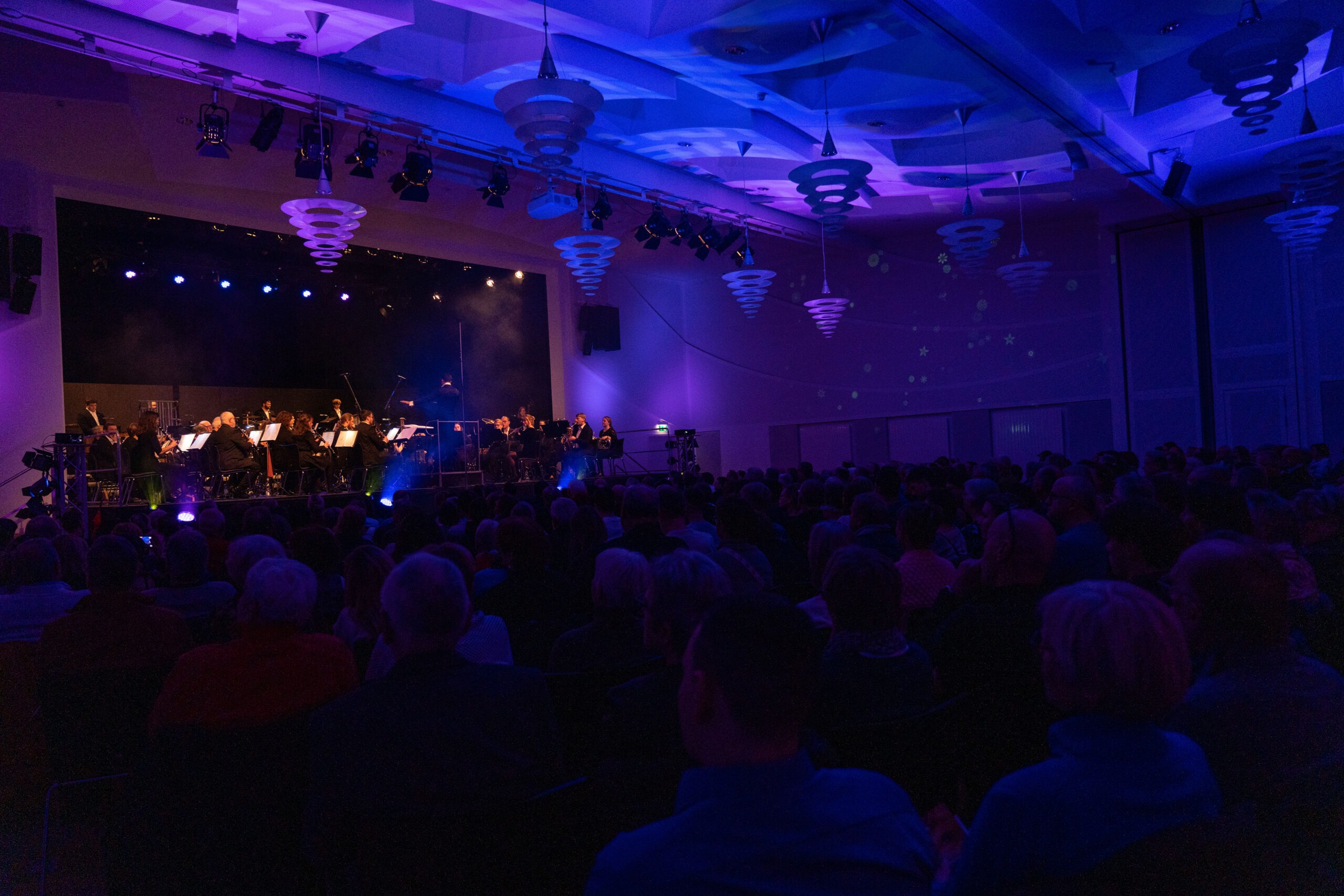 Ein blau beleuchteter Konzertraum mit einem Orchester auf der Bühne