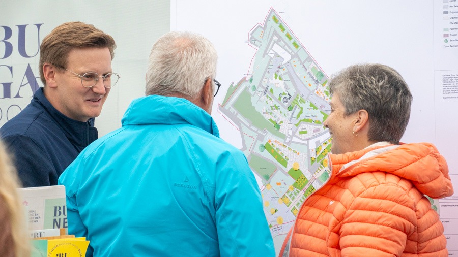 Ein Mann erklärt einem anderen Mann und einer Frau lächelnd einen Lageplan
