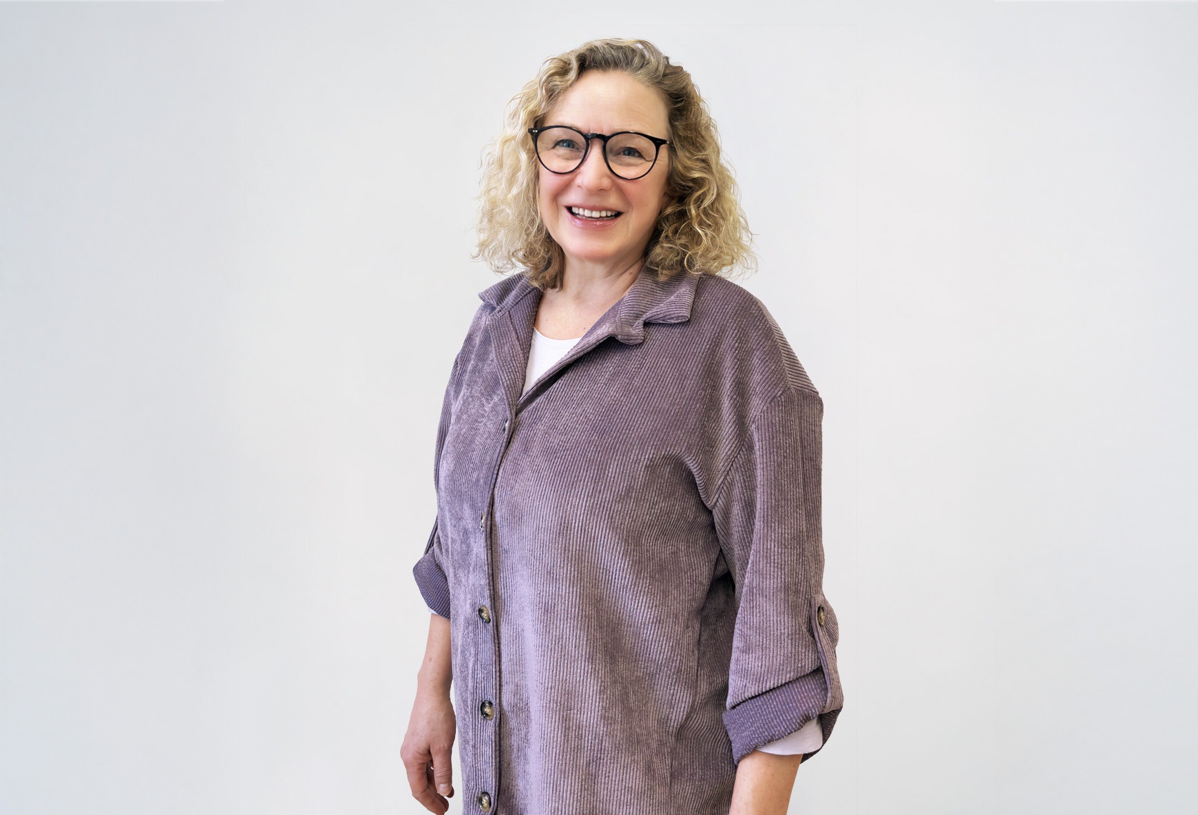 Eine blonde, lächelnde Frau in einem violetten Cordhemd