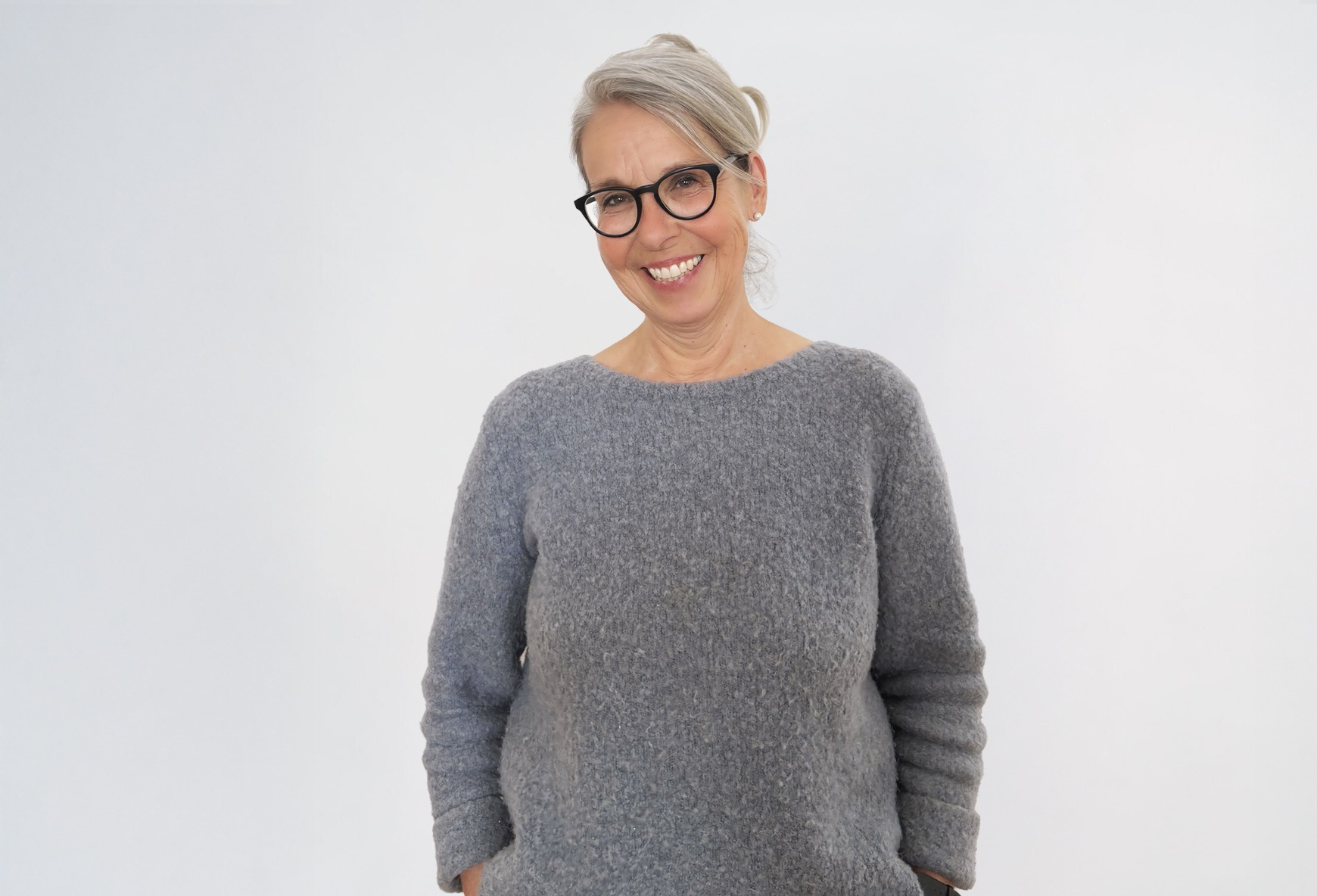 Eine blonde Frau in einem grauen Pullover lächelt.