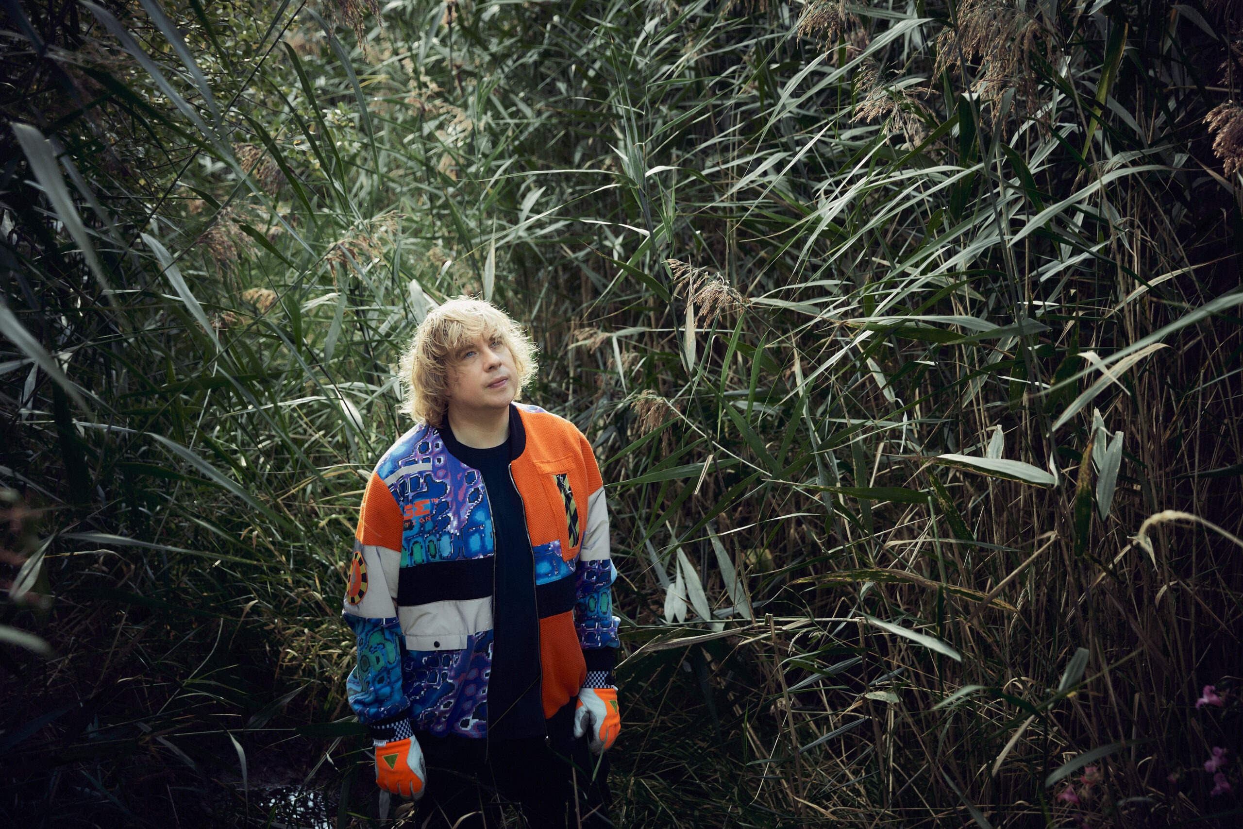 Ein Mann steht inmitten dichter Schilfrohre und blickt nachdenklich nach oben