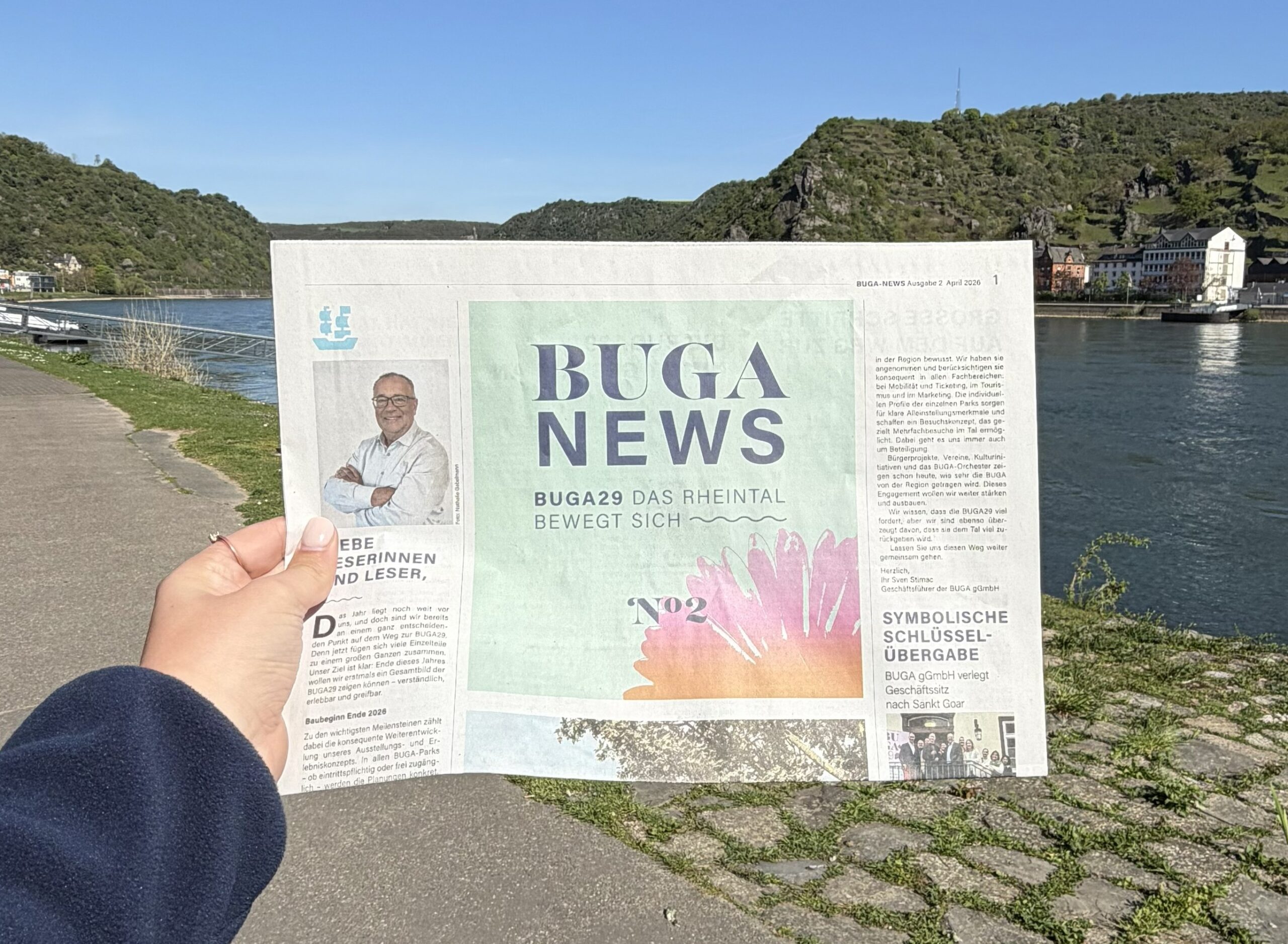 eine Hand hält die BUGA-Zeitung vor einem blauen Himmel hoch