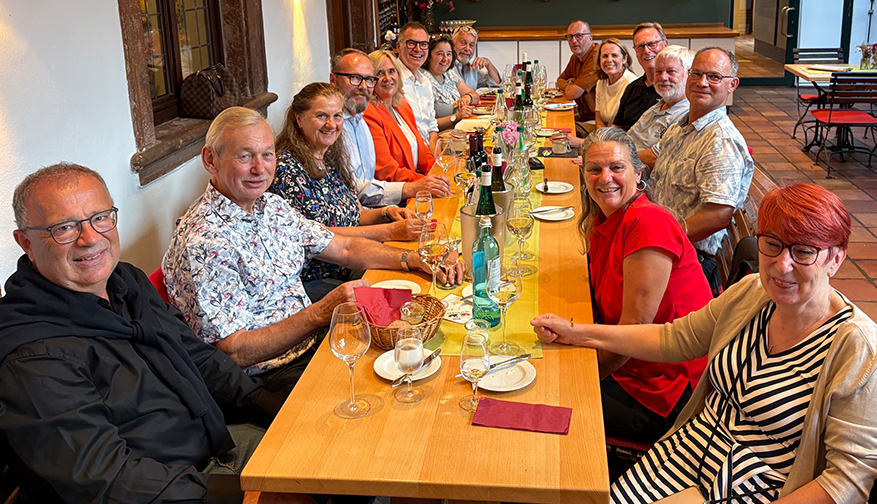 Teilnehmende eines Treffens der Fördervereine sitzen gemeinsam an einer langen gedeckten Tafel.